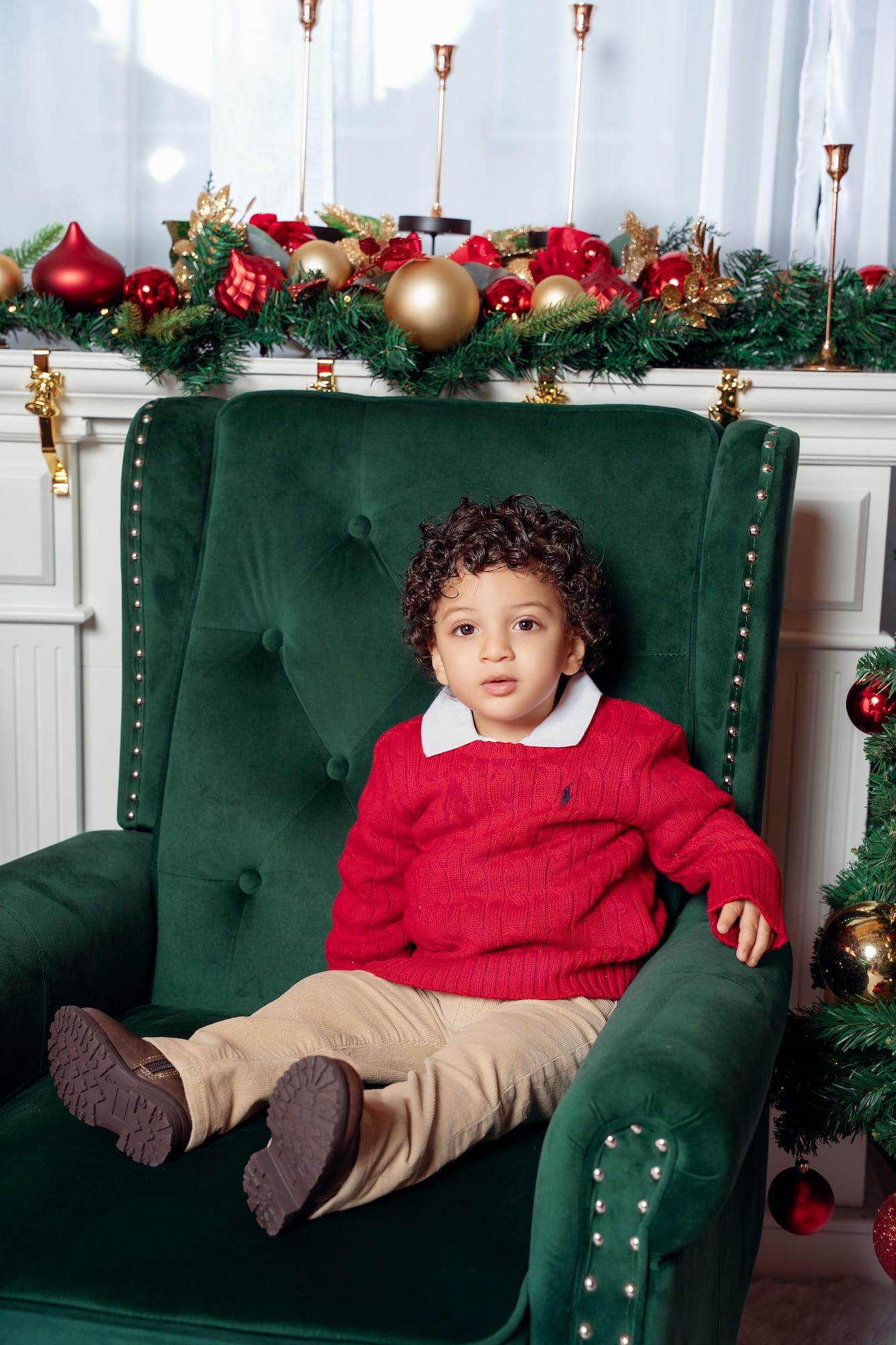 Boy sitting in a chair beside a Christmas tree and glowing fireplace