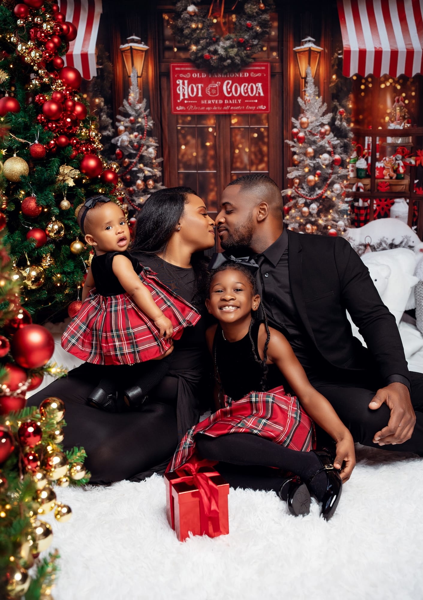 Family sharing a kiss beside Christmas gifts and a decorated tree