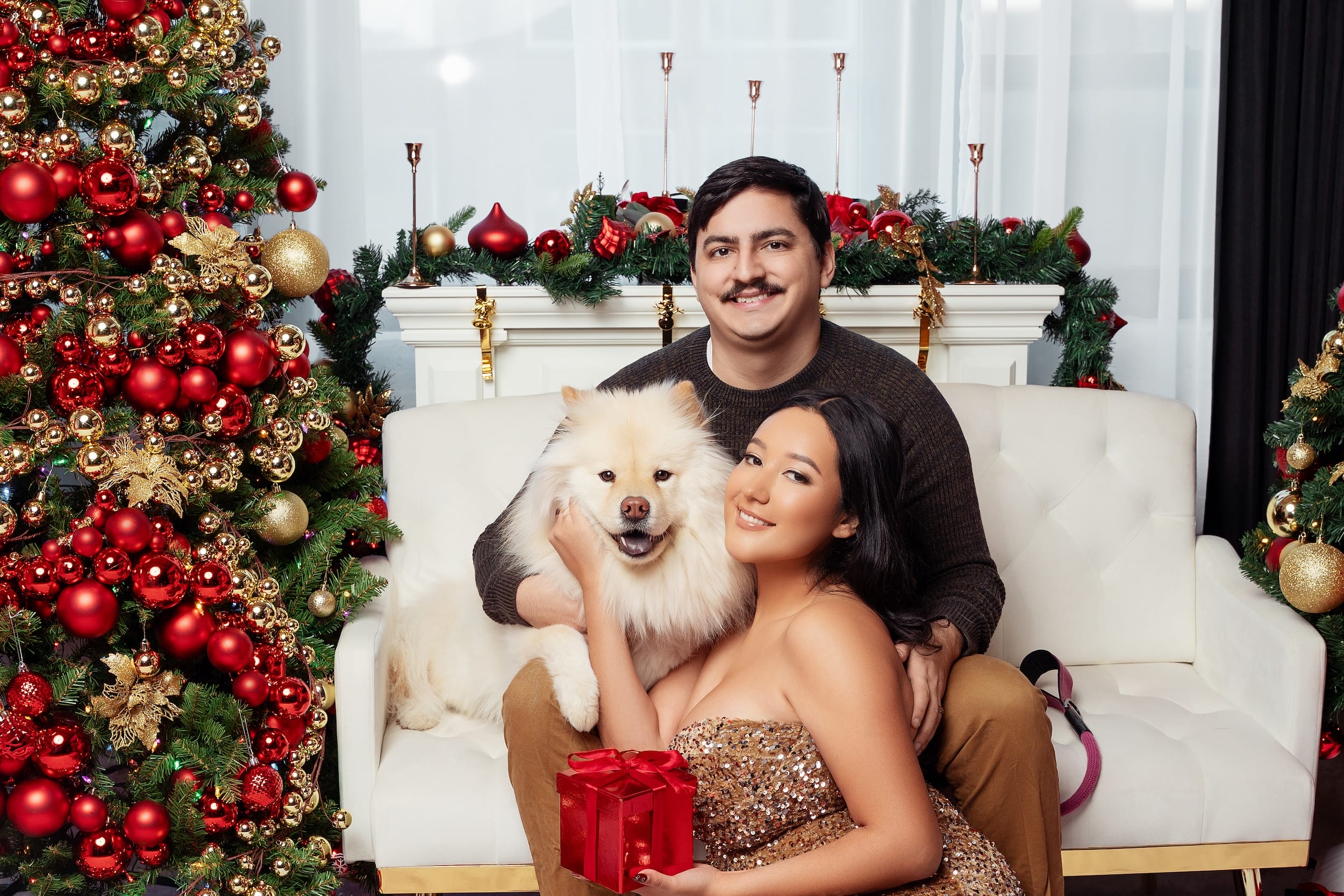 Couple with their dog holding a Christmas gift by the fireplace